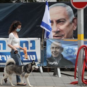 Valreklam hänger runtom i landet – många planscher föreställer Netanyahu. En kvinna med munskydd vandrar i Jerusalem förbi valaffischer föreställande Benjamin Netanyahu.