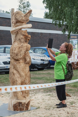 Minna Haveri fotograferar Leevi Halonens verk. Rastapäinen nainen ottaa valokuvaa karhun mallisesta puuveistoksesta
