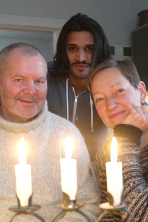 Frank Hellgren, Ahmed Aljuaifari och Pia Rousku poserar bakom en ljusstake med tre tända ljus i familjens kök