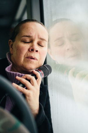 Katja Küttner istuu bussissa ja nojaa uupuneena, silmät kiinni ikkunaan. Kädessään hänellä on mikrofoni.