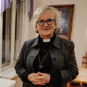 En kvinna i glasögon, grå jacka och svart tröja med prästkrage. Hon heter Monica Cleve.