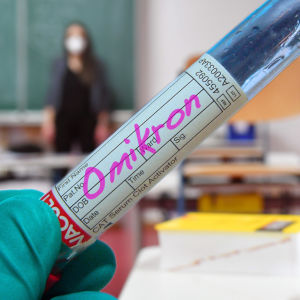 Ett teströr med ordet omikron skrivet på en klisterlapp med en skolklass och en lärare i bakgrunden.