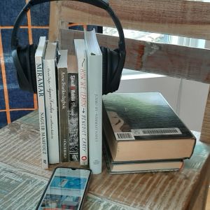 Författare får låneersättning när den fysiska boken lånas ut. Ersättningen för en utlånad e-bok eller ljudbok kommer via ett licensavtal. Boktrave på en stol med hörlurar spända runt sig och en mobiltelefon liigande bredvid.