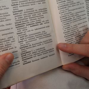 Kaksi kättä pitelee sivistyssanakirjaa, jonka aukeamalla k-kirjaimella alkavia sanoja.