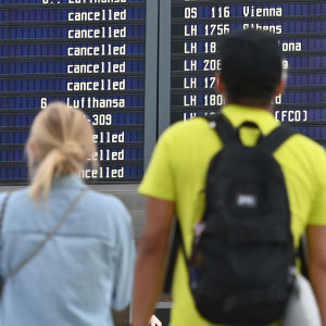 Tre personer står och tittar på en tavla på en flygplats där det står "inställt" vid många flyg.