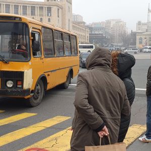 Buss åker förbi människor som står och väntar på grönt ljus på Republikens plats i Jerevan.