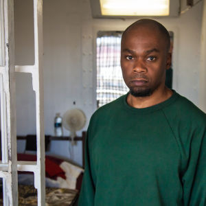 En intagen klädd i grön skjorta står vid gallret till sin cell i Atticafängelset i USA.