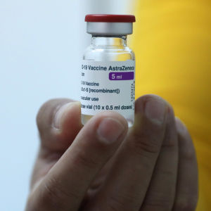 Finland stoppar inte användningen av vaccinet i nuläget. En hand som håller i en vaccinlaska.