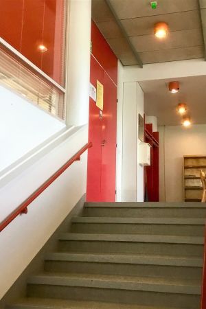 Biblioteket finns på andra våningen. Interiör i Fokus i Karis. Vita väggar, röda trappräcken och dörrar. Grått innertak som ser smutsigt ut.