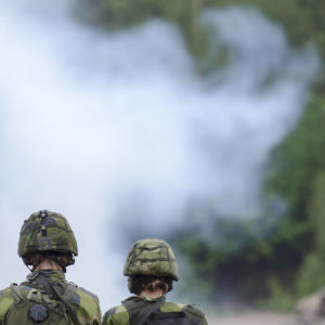 Soldater i stridsmundering står framför rök. De svenska soldater deltar i ett slutprov 2014.