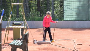 Barbro Wikberg har många järn i elden. Här vattnar hon en av tennisbanorna i Hangö. En kvinna på tennisplan. Hon spelar inte utan har just vattnat planen. Vattenslangen ligger på marken.