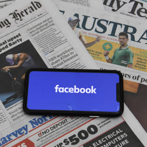 En mobiltelefon med texten facebook på skärmen. Mobiltelefonen ligger på en hög med tidningar från Australien.