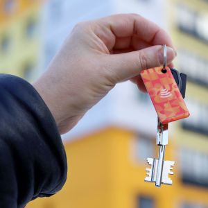 A closeup of a person holding a set of keys in their hand in front of a block of flats