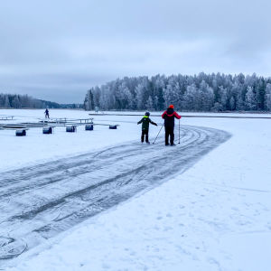 Två personer åker bortåt från kameran på en isväg över isen.