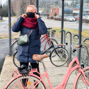 En kvinna sätter på sig ett munskydd. Hon står utomhus vid en cykelställning.