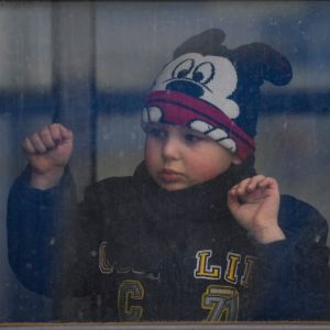 En pojke i mussepiggmössa tittar ut genom ett smutsigt tågfönster.