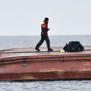 En räddnignsarbetare står på ett kapsejsat fartyg.