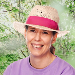 Kvinna i hatt mot somrig bakgrund.