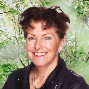 Tiina Lindfors ler rakt in i kameran. I bakgrunden syns en grönskande trädgård.