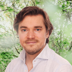 Dimitri Qvintus småler mot kameran. I bakgrunden syns en grönskande skogsdunge.