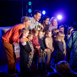 Fyra barnprogramledare står tillsammans med ett gäng barn och poserar framför kameran.