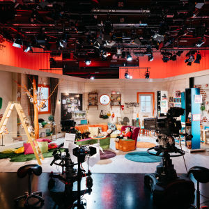 tv-studiossa lastenohjelman kulissit, etualalla tv-kameroita, katossa ja sivuilla valaisimia 
