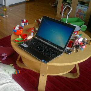 Laptop i vardagsrum fyllt av leksaker.