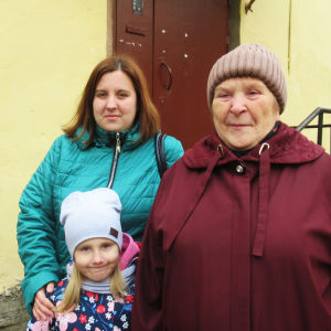 Tre kvinnor i Sankt Petersburg från tre olika generationer poserar vid ett gult stenhus. 