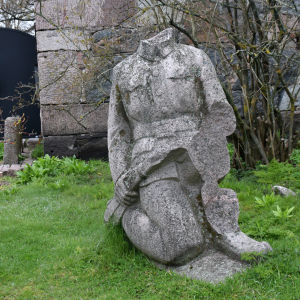 En skulptur som ser ut som en soldat men utan huvud står i en trädgård.