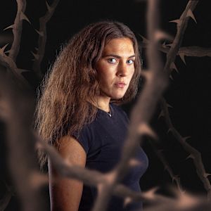 Martha Antonette Solli, programledaren för Nordens söner med taggiga buskar i förgrunden och bakgrunden. 