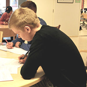 Elever sitter vid ett bord och skriver på papper
