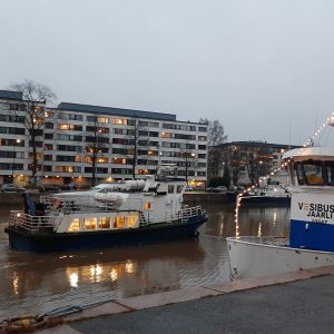 En blåvit sjöbuss, M/S Hamnskär, åker förbi en annan sjöbuss, M/S Jaarli, i Aura å i Åbo en smådimmig morgon.
