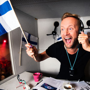 Mikko Silvennoinen selostuskopissa Suomen lippu kädessä.