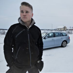 Porträttfoto av Oliver Majors med bil i bakgrunden