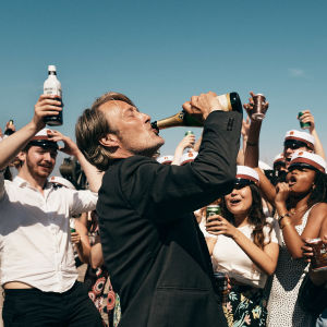 Martin (Mads Mikkelsen) dricker direkt ur en champangeflaska medan unga studenter jublar runtom honom.