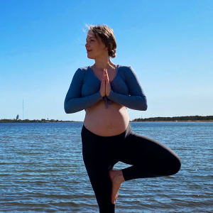 En kvinna med gravidmage som står i en yogaposé med vatten och öar i bakgrunden.