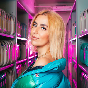 Renaz Ebrahimi seisoo sivuttain kameraan ja katsoo olkansa yli suoraan kohti.