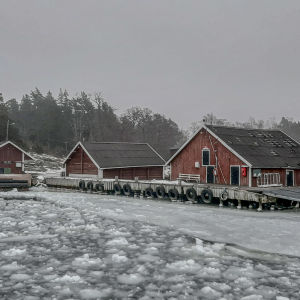 Själö förbindelsebåtsbrygga med röda byggnader i ett isigt vinterväder.