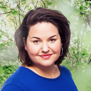 Daniela Franzell småler in i kameran framför en grönskande bakgrund.