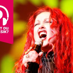 Cyndi Lauper blundar och sjunger i en mikrofon som hon håller i handen.