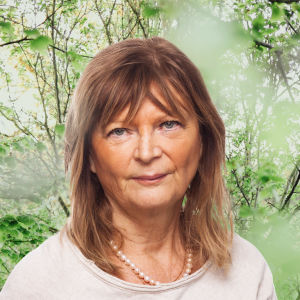 Annika Hällsten ser rakt in i kameran. Bakgrunden är en grönskande skogsdunge.