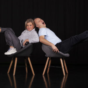 Jeanette Björkqvist och Magnus Londen sitter i två stolar i en svart miljö och spretar ut med benen åt varsitt håll. Jeanette tittar in i kameran och Magnus gäspar stort.