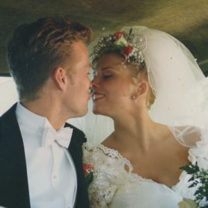 Huntuun ja morsiuspukuun pukeutunut Helena Ahti-Hallberg suutelee tuoreen aviomiehensä Ericin kanssa hääauton takapenkillä.