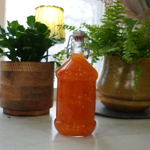 Makea ja kirpeä chilikastike pullossa työtasolla vihreiden kasvien vieressä.