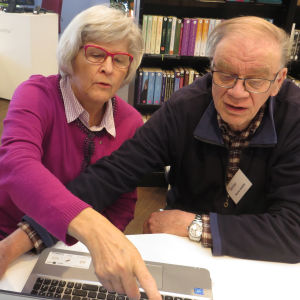 Enter-järjestön vertaisopastaja Raimo Anttila kirjastossa tietokoneen takana, opastettavana Irma Pantzar.