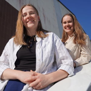 På bilden två unga kvinnor poserar i en trappa i solljus. De står på en trappa och tittar och ler mot kameran.