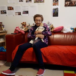 vanha nainen rutistaa nukkea sylissään punaisella sohvalla