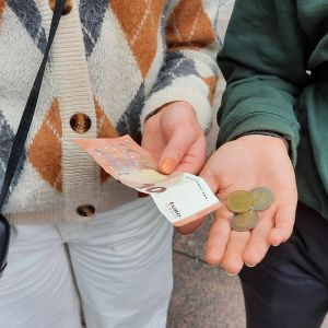 Kaksi ihmistä pitää kädessään rahaa. Toisella on 10 euron seteli ja toisella on kolikoina 4,50.
