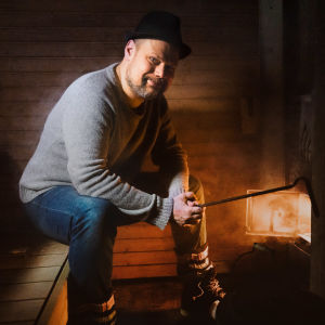 Toimittaja Olli Haapakangas lämmittää saunaa kiukaan edessä.