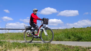 De första elcyklarna kom till Finland för över tio år sedan. En kvinna åker på en elcykel. I bakgrunden syns blå himmel och grönt gräs.